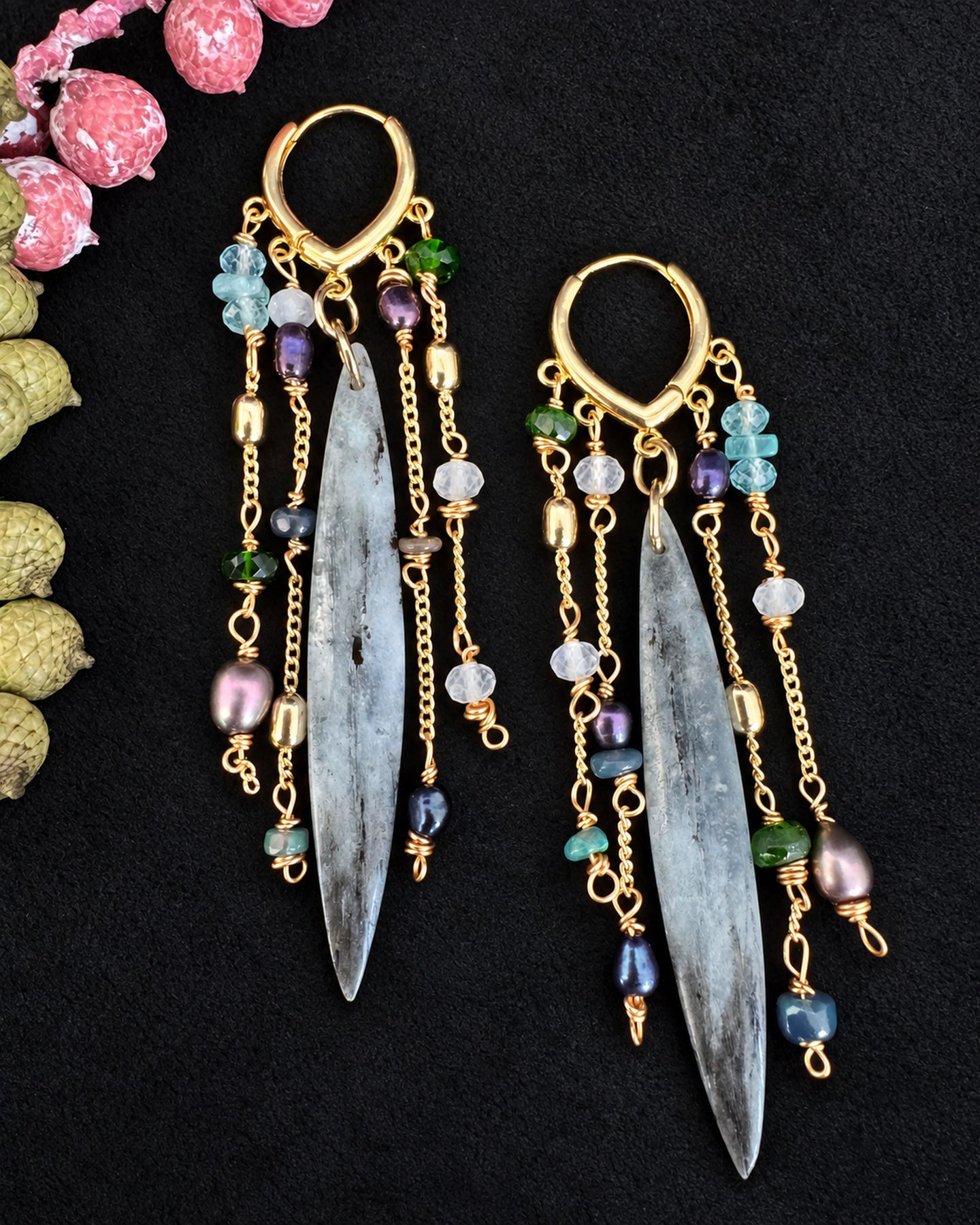Angled close view of gold-toned chains, pale blue and green accents and grey-blue pendants, with parts of the earrings extending beyond the frame.