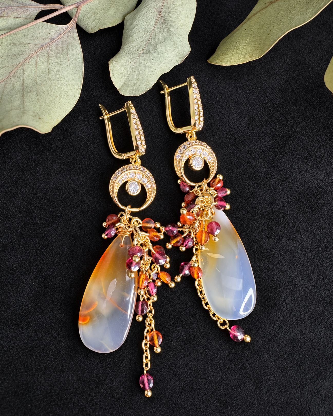 Flat view of the earrings showing gold-toned fastenings, circular connectors and pale translucent drops with yellow and orange markings.