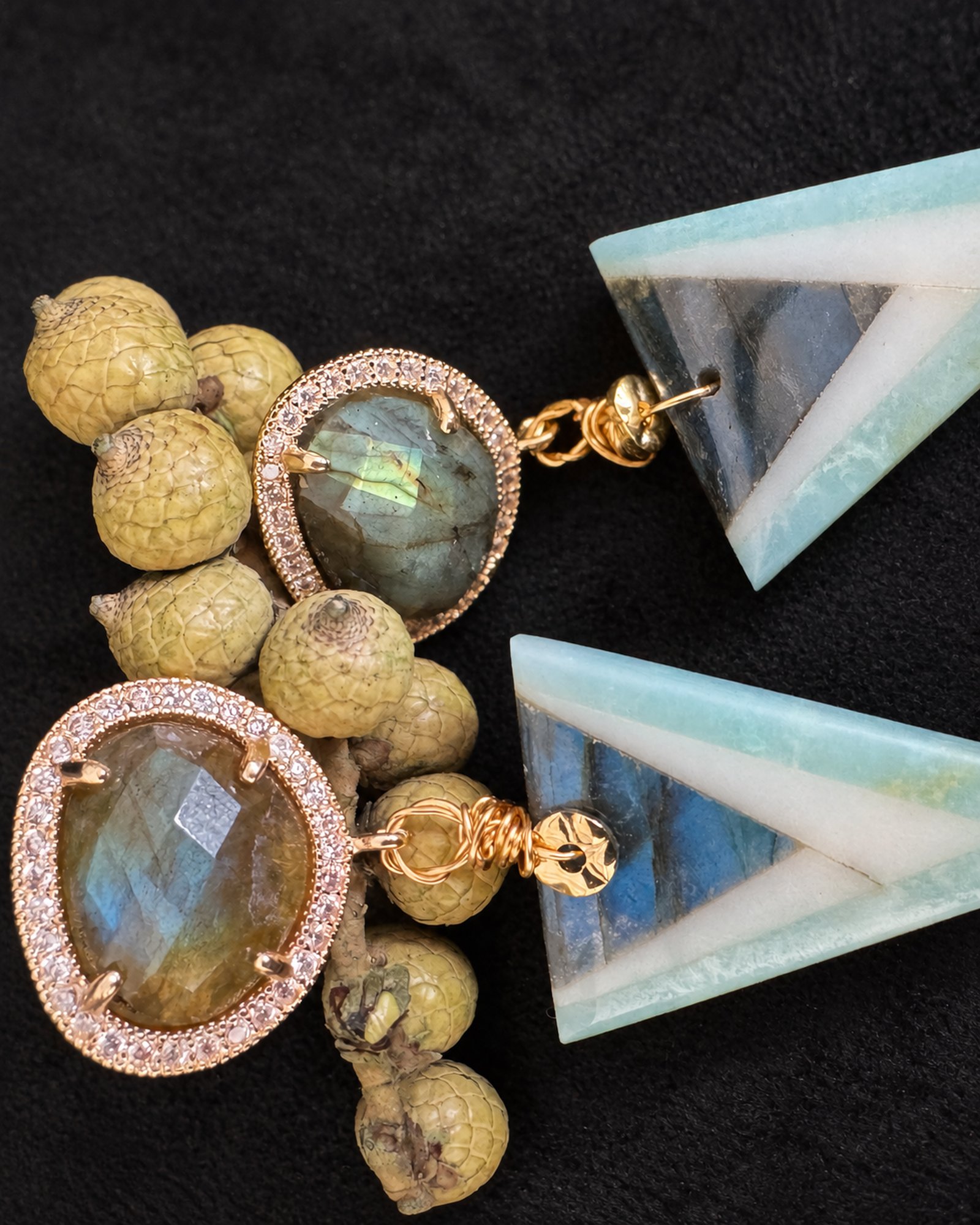 Sideways detail of oval halo tops and triangular drops beside gold-coloured seedpods, with the drop tips outside the frame.