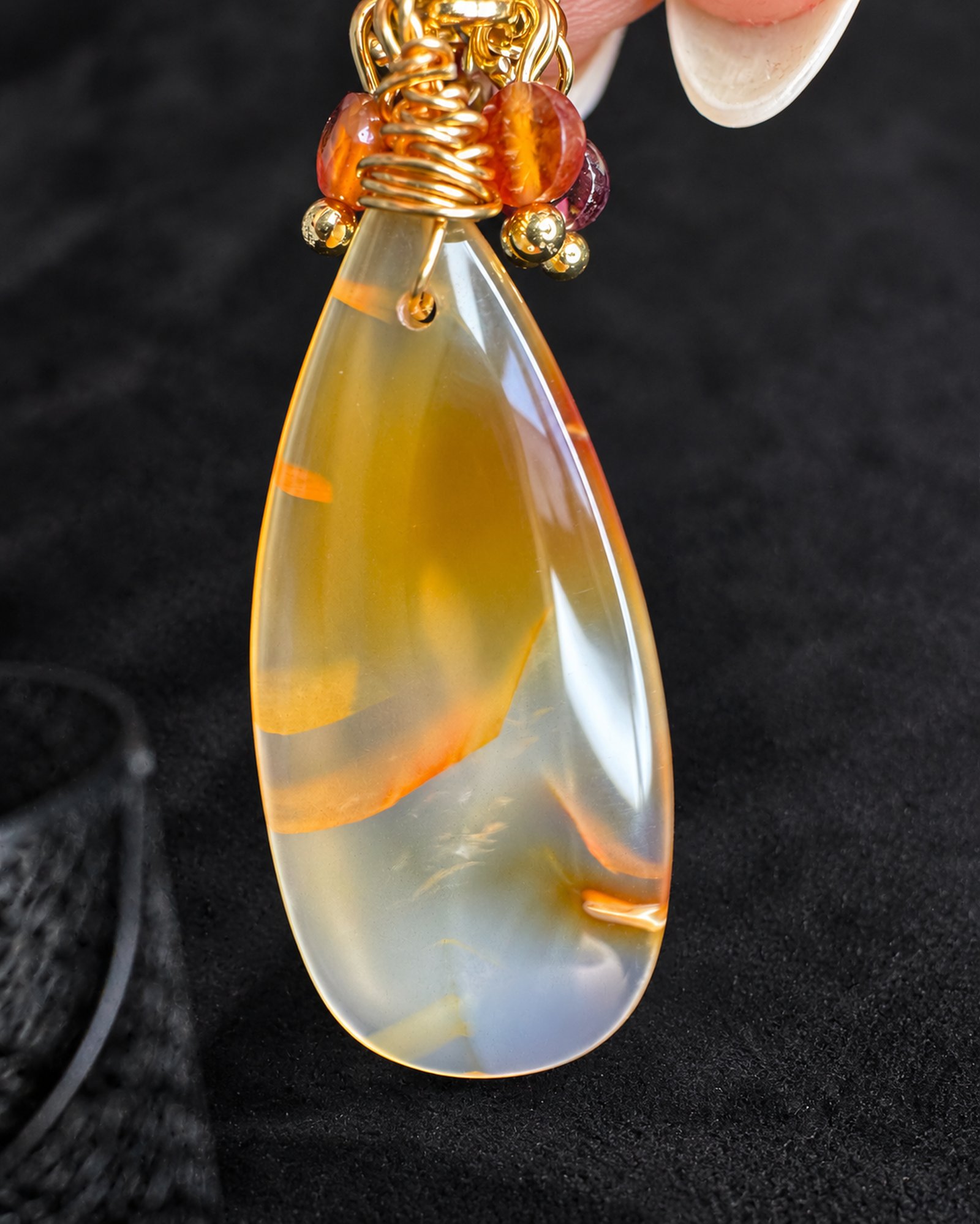Close-up of a smooth translucent teardrop with honey-yellow areas, curved orange markings and gold-toned wire wrapping.