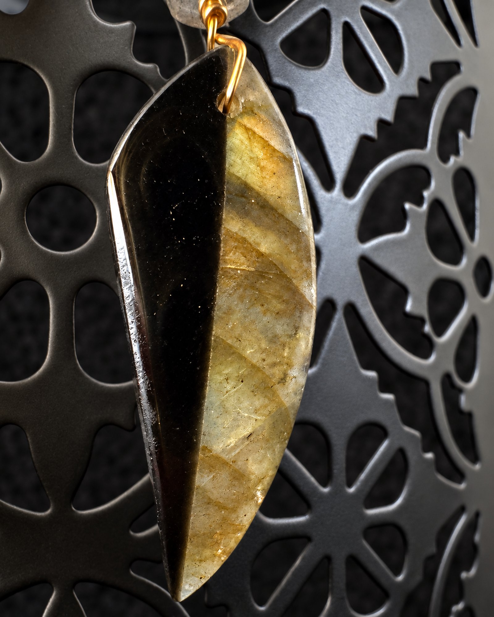Close view of the curved leaf-shaped drop with a black section and muted olive-gold surface.