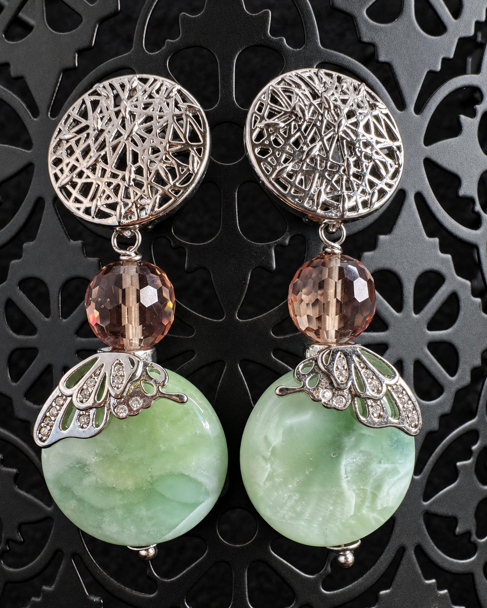 Sage Larissa earrings with circular silver-toned openwork tops and mottled pale green round drops on a dark patterned display.