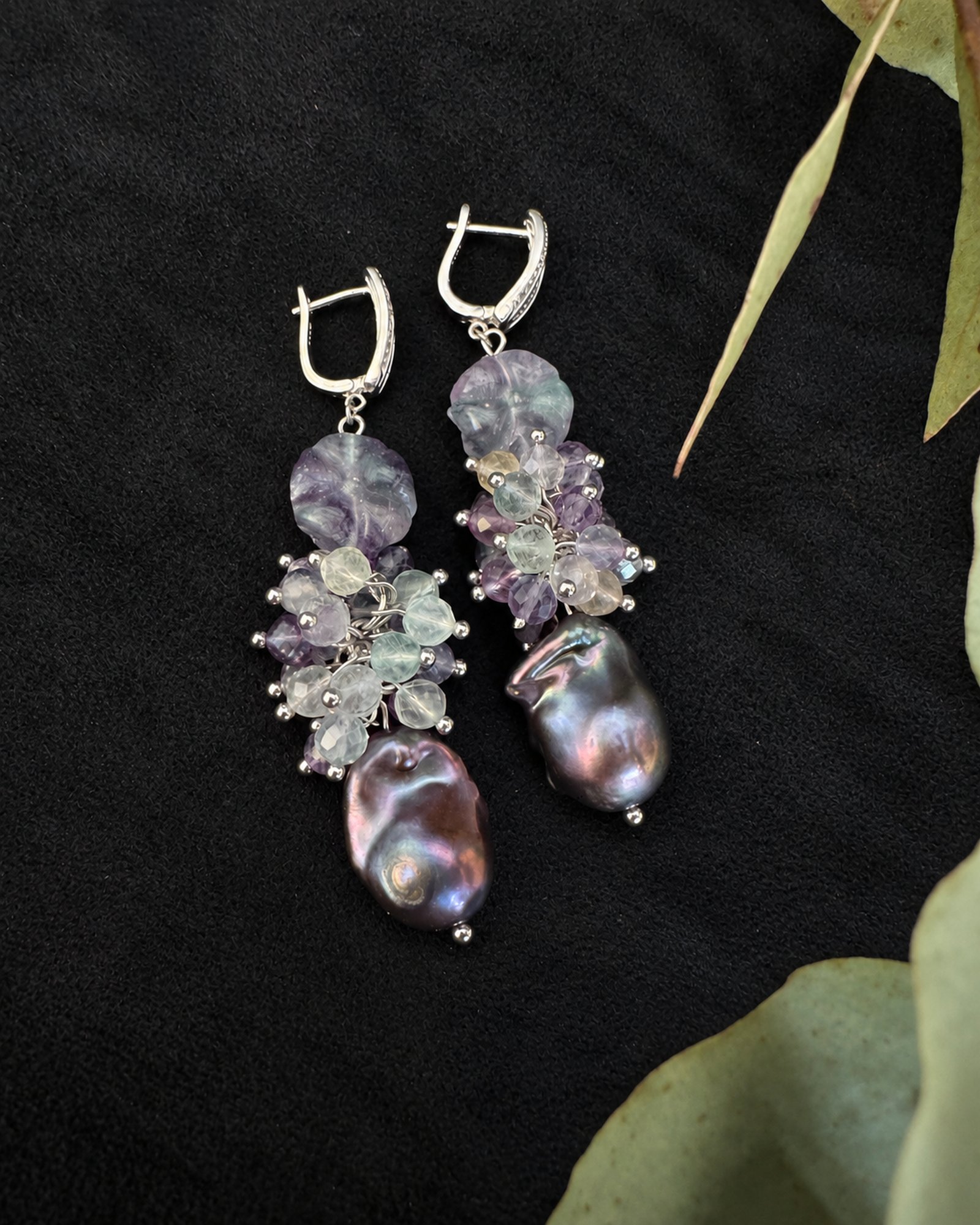 Reverse view of both earrings laid flat on black fabric, with open fastenings and iridescent drops.