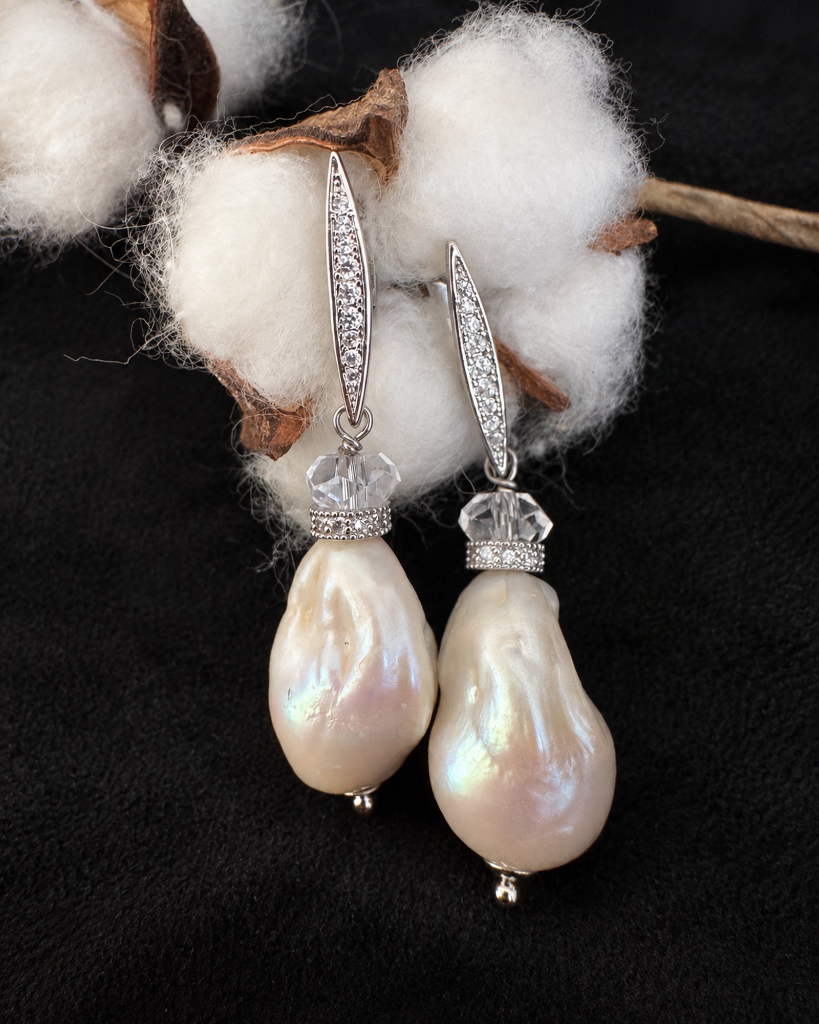 Ivory-coloured drop earrings arranged at staggered heights beneath cotton stems against a black background.