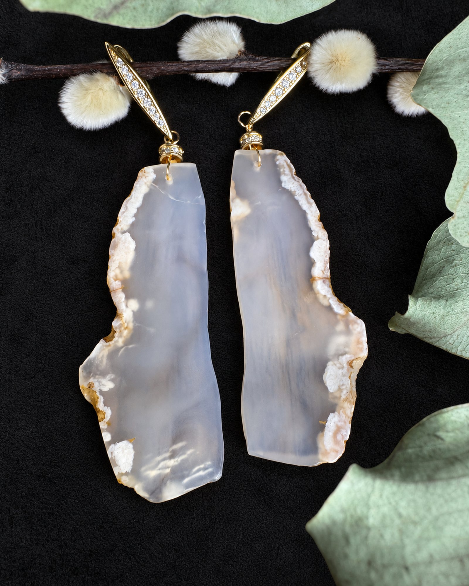 Flatlay of pale grey earrings with distinct asymmetric outlines, cloudy markings and elongated gold-coloured fittings.