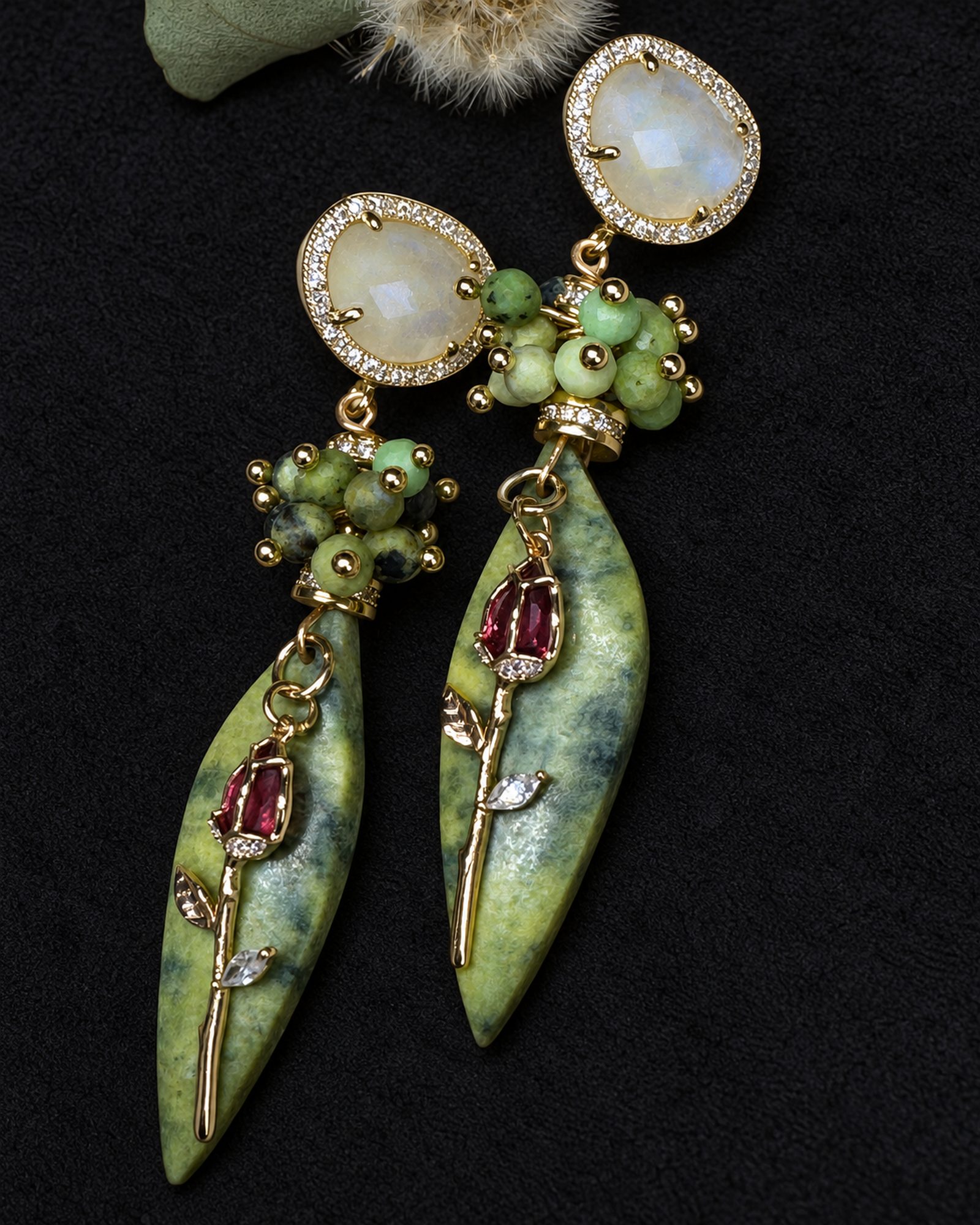 Both earrings arranged diagonally on a dark background, showing pale round tops, green bead clusters and pointed leaf-shaped drops.