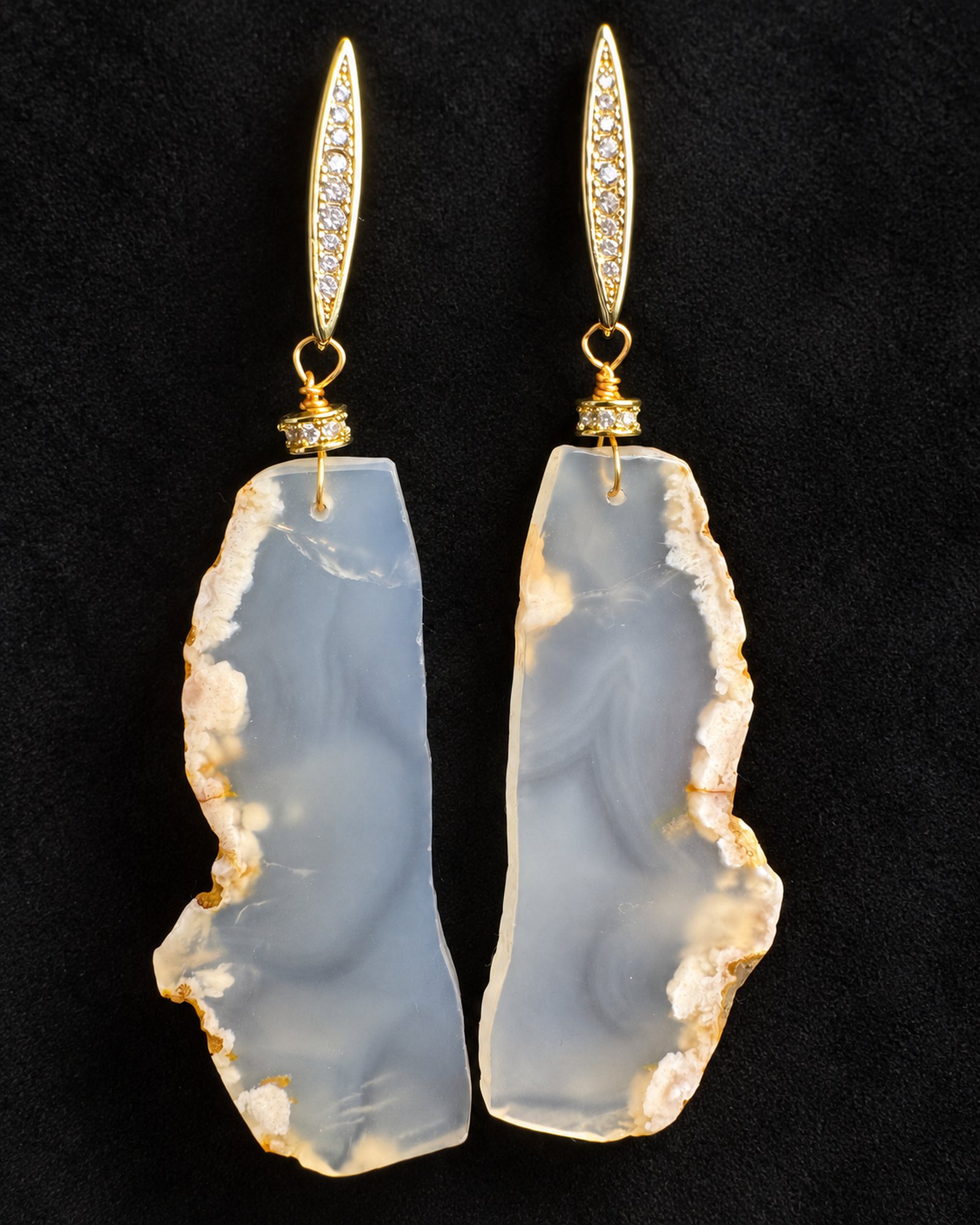 Hanging view of long, irregular pale grey earrings with cloudy white markings, gold-coloured borders and pointed fittings.