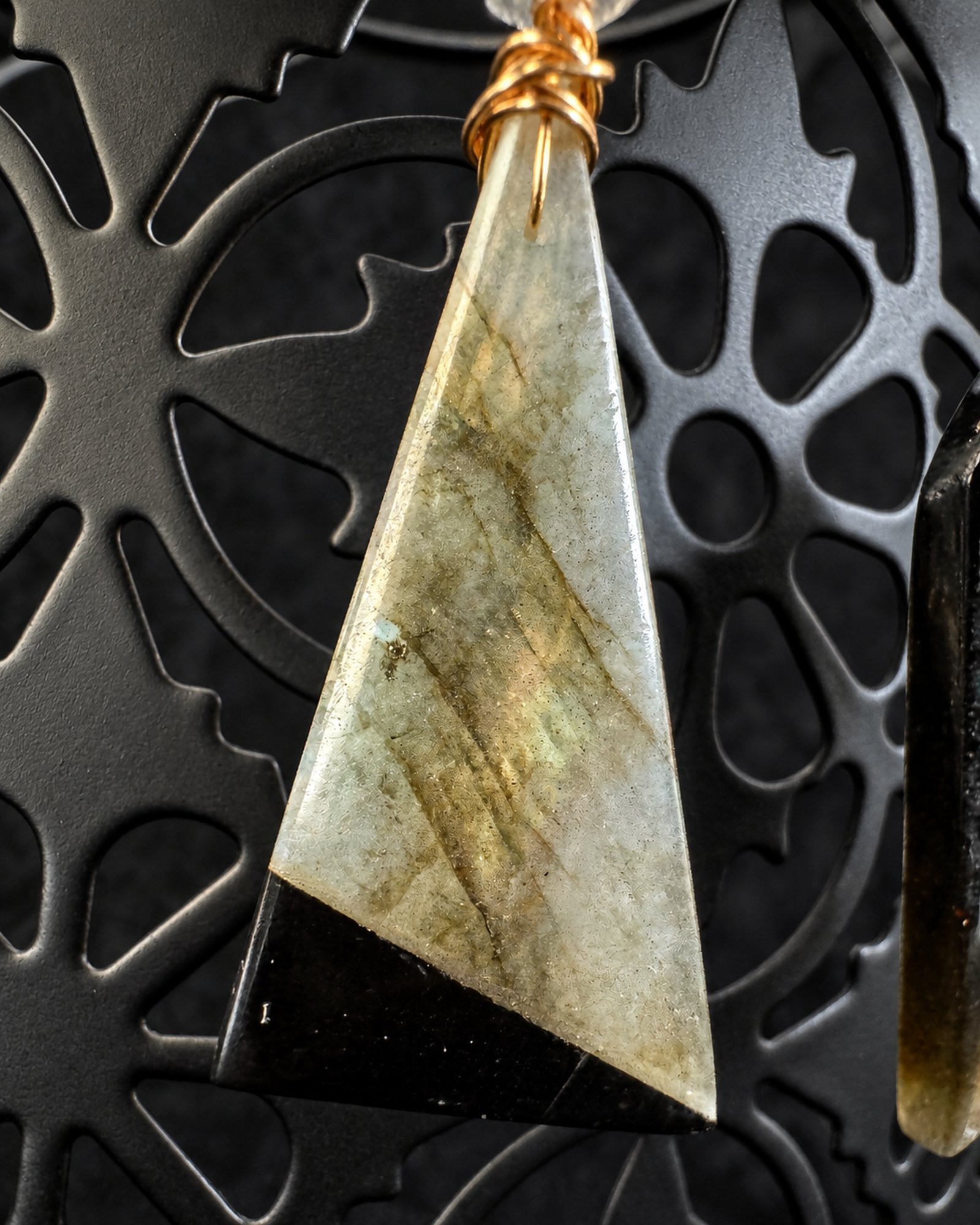 Close view of the triangular drop, showing pale grey-green mottling, a black diagonal end section and gold-toned wire attachment.