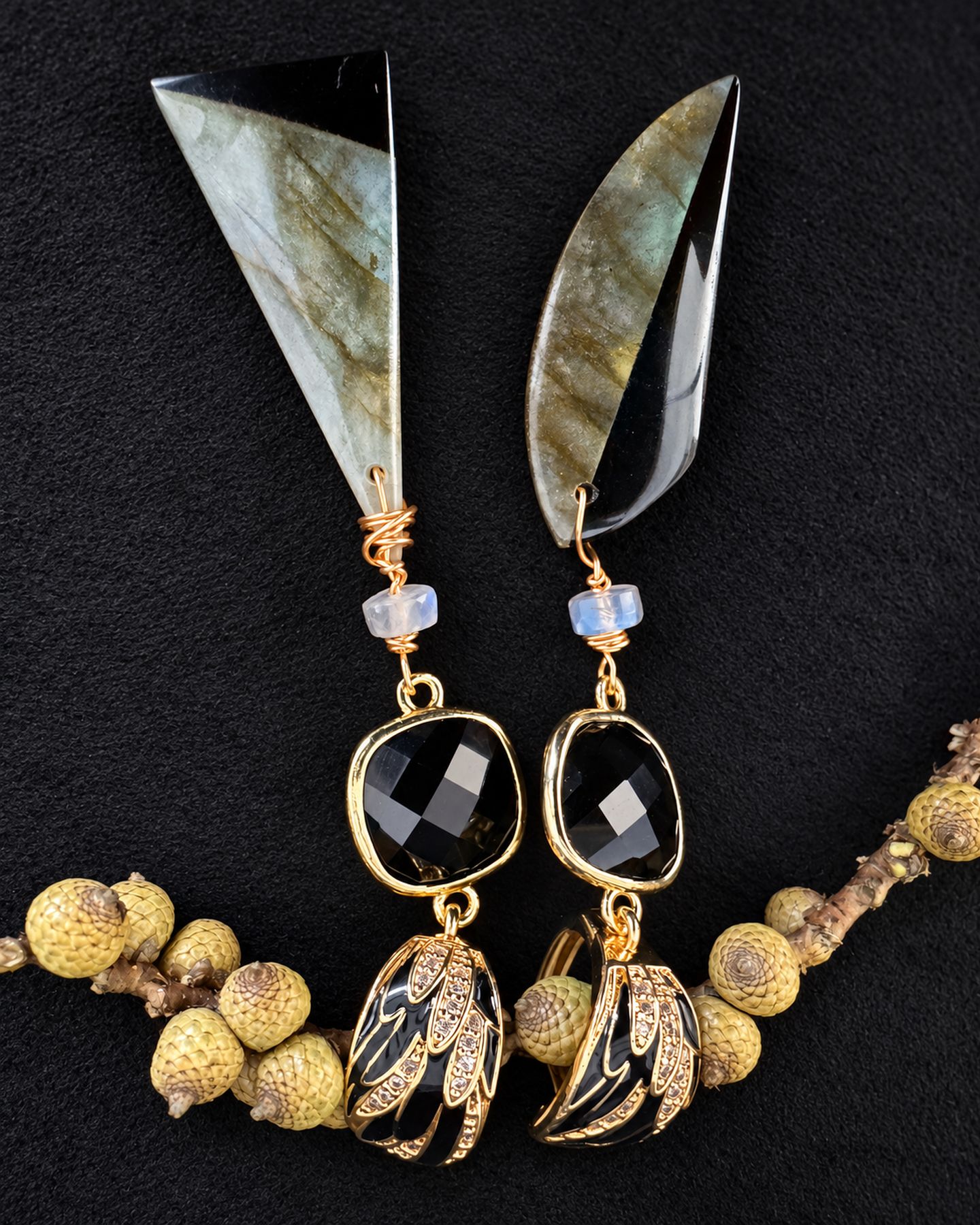 Both earrings laid flat with their long drops pointing upward and a yellow botanical branch beneath.