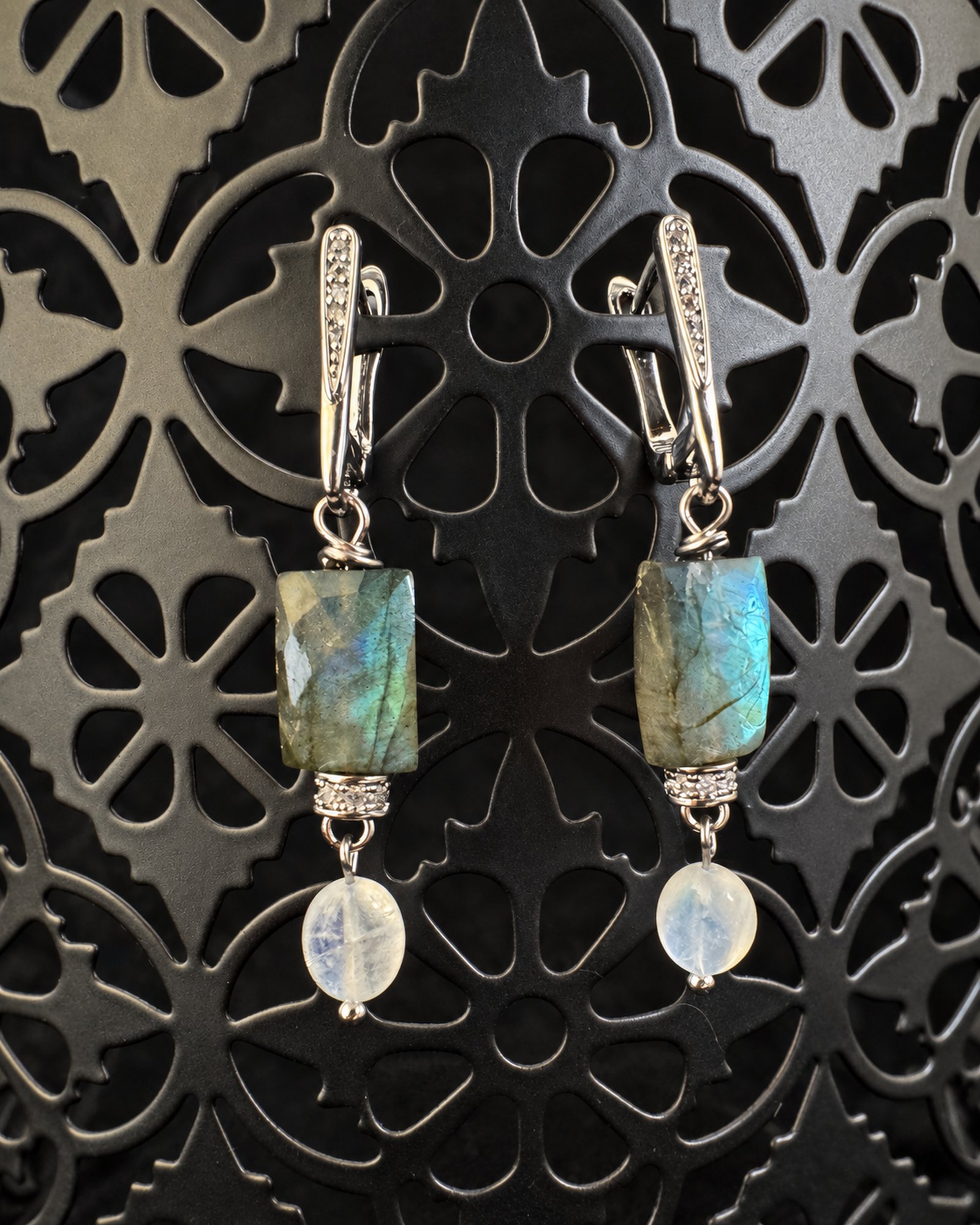 Pair of grey-green and blue drop earrings with pale translucent oval drops and silver-toned fastenings on an ornate openwork display.