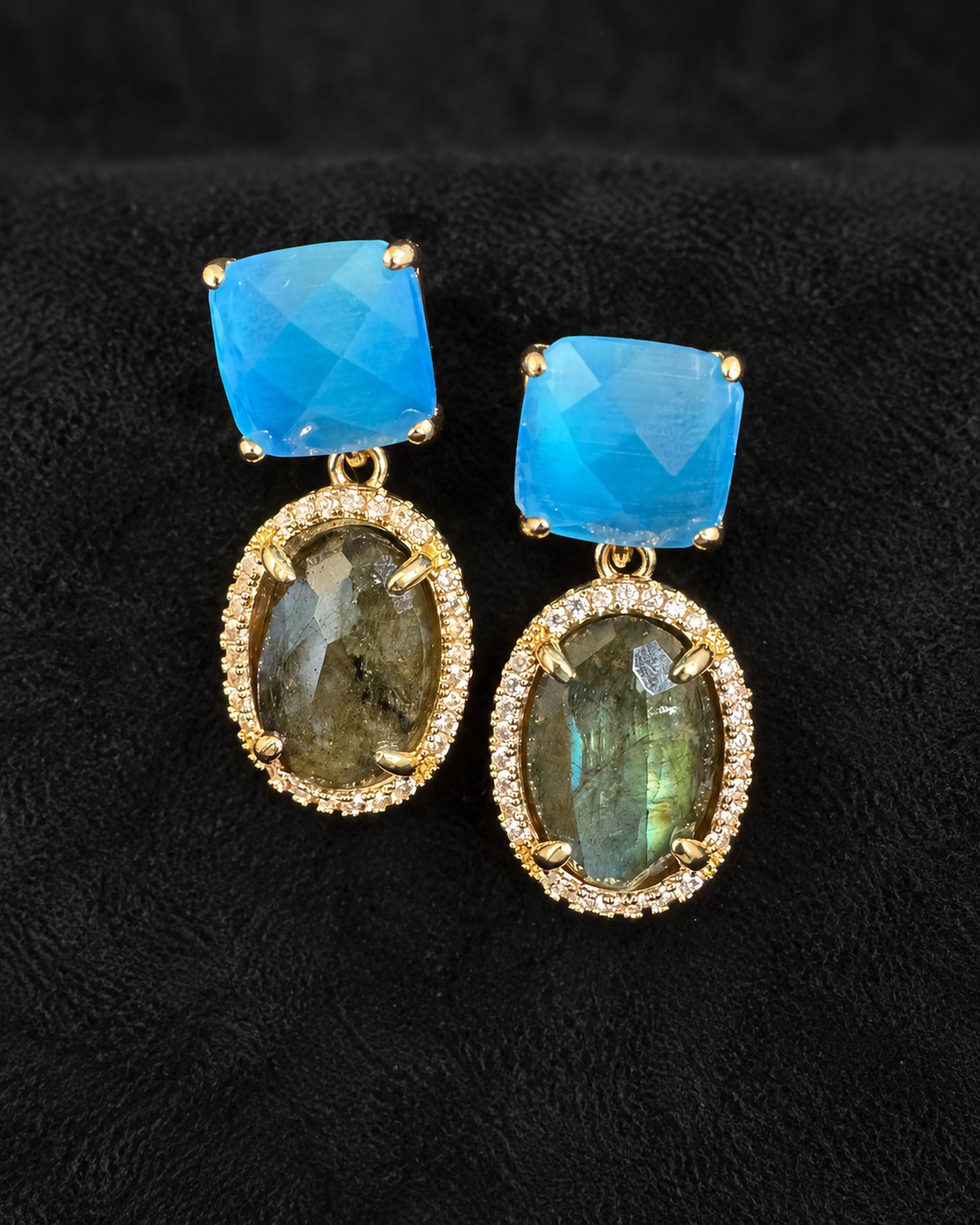 Pair of drop earrings with cyan cushion-shaped tops and smoky grey-green oval drops in gold-toned borders against black.
