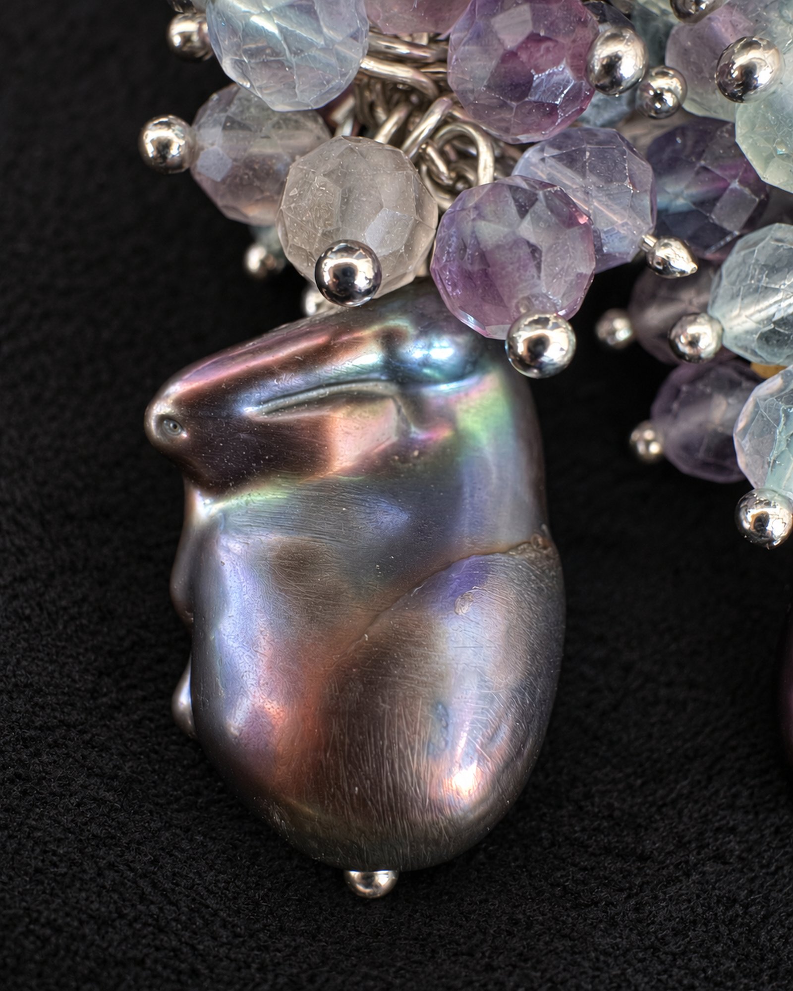 Close-up of an irregular dark drop with blue, green and pink reflections beside a partial bead cluster.