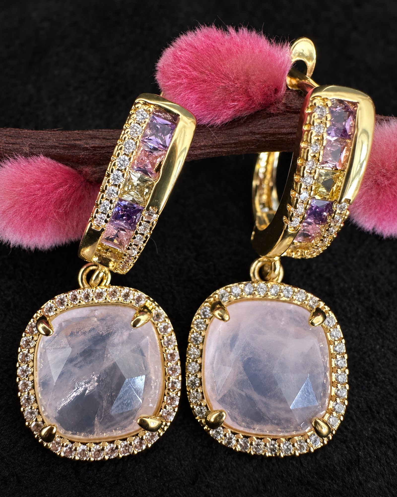 Close-up of cushion-shaped smoky lilac drops, clear accent borders and decorated gold-toned hoops.