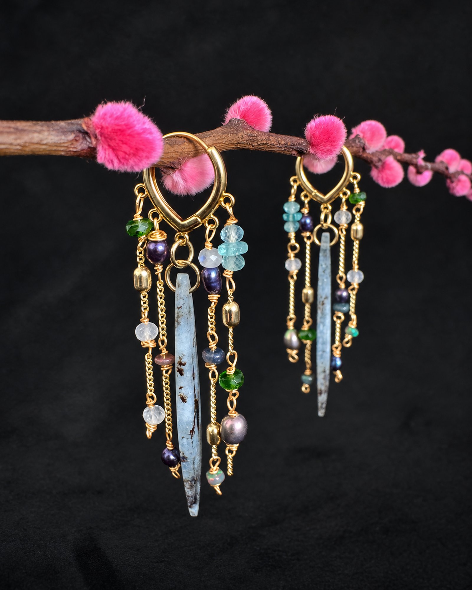 Long earrings hanging from a pink flowering branch, with grey-blue pendants and small multicoloured accents.
